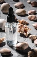 contagocce di olio essenziale per la cura della pelle in una bottiglia di vetro vicino a conchiglie e ciottoli