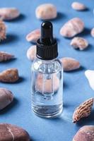 contagocce di olio essenziale per la cura della pelle in una bottiglia di vetro vicino a conchiglie e ciottoli