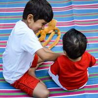 Due contento ragazzi nel società parco, contento asiatico fratelli chi siamo sorridente felicemente insieme. fratelli giocare all'aperto nel estate, migliore gli amici. bambino piccolo bambino ragazzo giocando con il suo contento fratello nel il giardino foto