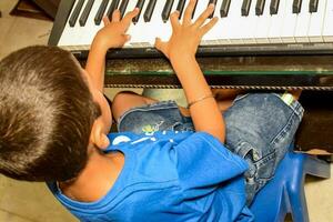 asiatico ragazzo giocando il sintetizzatore o pianoforte. carino poco ragazzo apprendimento Come per giocare pianoforte. del bambino mani su il tastiera interno. foto