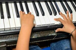 asiatico ragazzo giocando il sintetizzatore o pianoforte. carino poco ragazzo apprendimento Come per giocare pianoforte. del bambino mani su il tastiera interno. foto