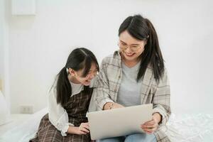 asiatico famiglia sorridente madre e figlia uso il il computer portatile shopping in linea insieme contento momento foto