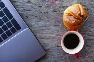 tazza di caffè rosso e gustoso panino con computer portatile sul tavolo di legno foto