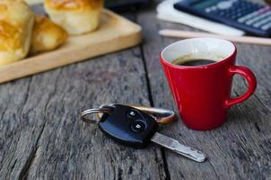 tazza rossa del caffè espresso e chiave dell'automobile sul fondo della tavola in legno foto
