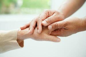 badante che si tiene per mano paziente donna anziana asiatica, aiuto e cura in ospedale. foto