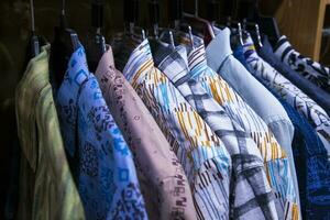 colorato varietà di camicie impiccagioni nel un' capi di abbigliamento showroom. chiuso messa a fuoco foto