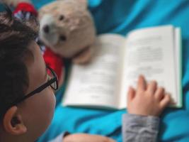 piccolo bambino che legge un libro a casa con il suo orsacchiotto giocattolo