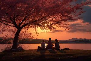 il silhouette di un' famiglia godendo un' picnic sotto un' ciliegia fiorire albero nel tramonto cielo. ai generativo foto