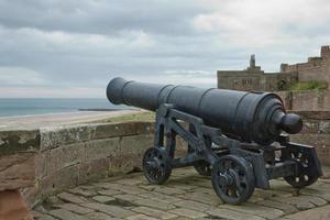 Il vecchio cannone di ferro al castello di Bamburgh sulla costa di Northumberland dell'Inghilterra, Regno Unito foto