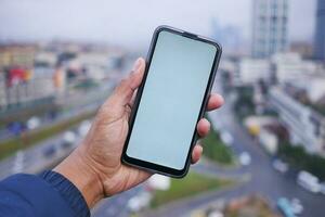 giovane uomo mano utilizzando inteligente Telefono con verde schermo contro città edifici foto