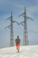 atleta corre nel il neve vicino alta tensione piloni foto