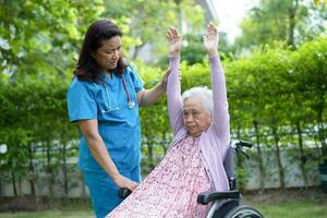 medico Aiuto e cura asiatico anziano donna paziente esercizio nel il mattina su sedia a rotelle a parco nel Ospedale. foto