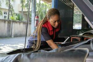 uno nero femmina professionale settore automobilistico meccanico lavoratore controlli un ev auto batteria e ibrido motore a un' Manutenzione box auto, esperto elettrico veicolo servizio, e fissaggio occupazioni auto industria. foto