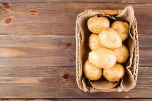 fresco giallo patate nel un' cestino su un' di legno sfondo. vegetariano cibo. superiore Visualizza. copia spase foto