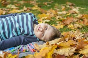 bambini giocare nel il autunno parco, in giro un' lotto di giallo le foglie. il ragazzo bugie nel il acero le foglie. autunno fogliame. foto