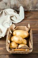fresco giallo patate nel un' cestino e stoffa su un' di legno sfondo. vegetariano cibo. verticale Visualizza foto