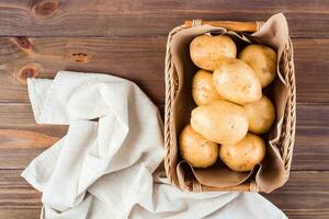 fresco giallo patate nel un' cestino e stoffa su un' di legno sfondo. vegetariano cibo. superiore Visualizza foto