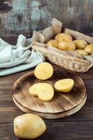 fresco giallo patate tagliare in pezzi su un' tavola e un' cestino con tuberi su un' di legno tavolo. vegetariano cibo. verticale Visualizza foto