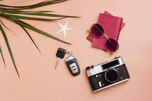 luminosa viaggio piatto posare con occhiali da sole, passaporti, Vintage ▾ telecamera e auto chiavi su un' beige sfondo. auto viaggio. superiore Visualizza foto