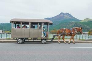 yufuin, oita, kyushu, giappone - ottobre 14, 2018 il turista su il cavallo carrozza cavalcata in giro Yufuin, fiume e yufu montagna sfondo foto