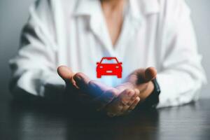 attività commerciale donna di mano proteggere rosso icona auto su scrivania. pianificazione per gestire mezzi di trasporto finanza costi. concetto di auto assicurazione attività commerciale, Salvataggio acquistare - vendita con imposta e prestito per nuovo macchina. foto