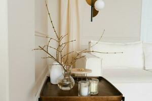 albero rami con introdotto mini cuffie nel un' bicchiere vaso e candele su un' di legno caffè tavolo. scandinavo vivente camera arredamento foto