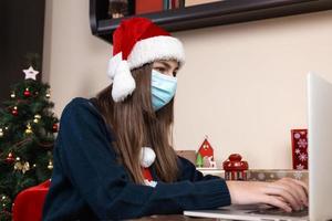 ragazza in cappello di Babbo Natale utilizzando laptop per videochiamata ad amici e genitori