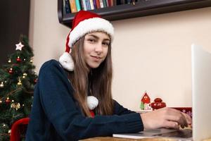 ragazza in colloqui di cappello di Babbo Natale utilizzando il computer portatile foto
