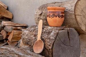 brocche in ceramica tradizionali e cucchiaio di legno sul tovagliolo decorativo contro l'albero di legno foto