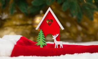 cervo di casa di legno del giocattolo di Natale e albero su un cappello da Babbo Natale e una coperta bianca che imita la neve