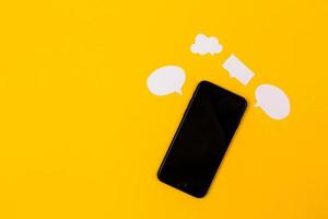 smartphone con bolle di discorso di carta su sfondo giallo foto