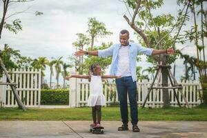 padre porzione sua poco figlia per cavalcata un' skateboard, poco ragazza e sua padre giocando con skateboard all'aperto, Il padre di giorno concetti foto