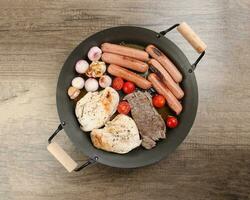 mescolare incontrare padella pollo Seno Manzo bistecca salsiccia pomodoro cipolla aglio olio friggere griglia su metallo frittura padella Due legna maniglia su rustico di legno sfondo foto