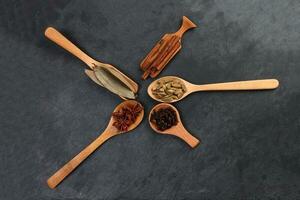 mescolare varietà Spezia cannella cardamomo Chiodo di garofano baia foglia di legno cucchiaio su nero ardesia sfondo foto