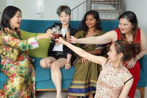 giovane sud-est asiatico donna gruppo parlare celebrare cantare fabbricazione divertente beffardo facce espressione potabile applauso Saluti su blu vivente camera divano foto