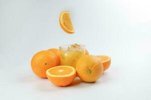 fresco giallo arancia succo nel bicchiere con totale galleggiante affettato arancia frutta e ghiaccio cubo su bianca sfondo foto