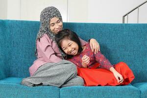 ritratto di sud-est asiatico malese madre figlia sedersi su blu divano parlare contento divertimento ridere. madre è adhd e bambino autismo autistico foto