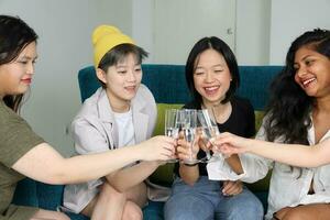 giovane asiatico donna gruppo parlare pettegolezzo Chiacchierare cantare bevanda Saluti festa divertimento godere emozione su blu vivente camera divano foto