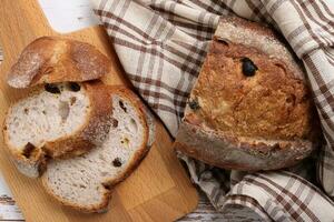 rustico totale grano artigiano pane pagnotta fetta con mirtillo Uvetta asciutto frutta noccioline avvolto nel dama stoffa con di legno chopping tavola al di sopra di tavolo superiore piatto posare Visualizza foto