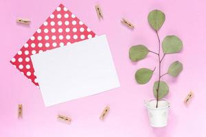 un rametto con foglie in un secchio bianco con un biglietto di auguri bianco su un semplice sfondo rosa foto