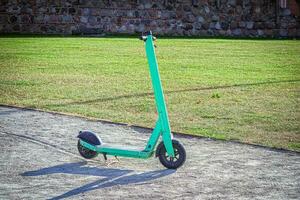 luminosa verde scooter in piedi nel il mezzo di un' strada vicino verde prato su soleggiato estate giorno foto