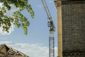 giallo mattone edificio angolo con di legno tetto e il contruction gru dietro a con un' verde albero frondoso ramo e blu cielo su il sfondo foto