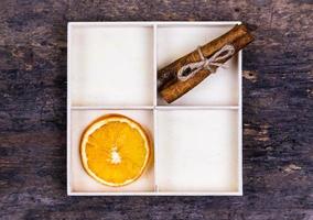 una scatola bianca con scomparti su uno sfondo di legno pieno di arance secche e bastoncini di cannella