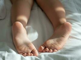 avvicinamento di spoglio piedi di un' bambino dire bugie su il letto. foto