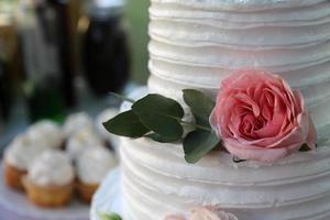 bella torta nuziale decorata con foglie e fiori freschi foto