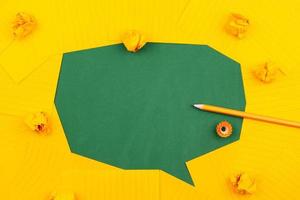 fogli di carta arancioni giacciono su un consiglio scolastico verde e formano una bolla di chat con la matita