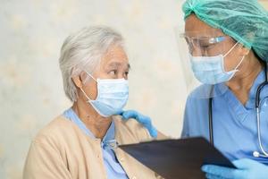 medico che utilizza lo stetoscopio per controllare il paziente asiatico anziano o anziano donna anziana che indossa una maschera facciale in ospedale per proteggere l'infezione covid 19 coronavirus foto