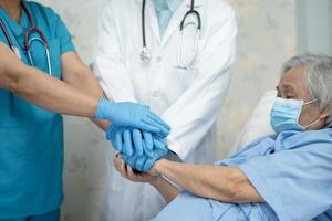 squadra di medici asiatici e paziente anziana signora impilano le mani insieme come squadra per la motivazione nuova normalità per il trattamento dell'infezione covid 19 coronavirus in reparto ospedaliero foto