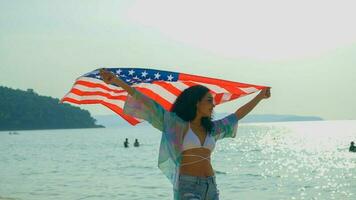 giovane donne hold americano bandiere su il spiaggia e il mare su loro estate vacanza e essi Sorridi e godere loro vacanza. foto