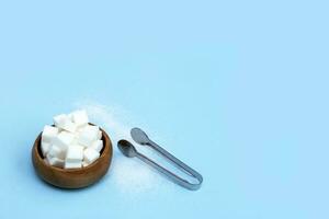 raffinato zucchero nel un' di legno tazza con zucchero pinza su un' blu sfondo con copia spazio foto